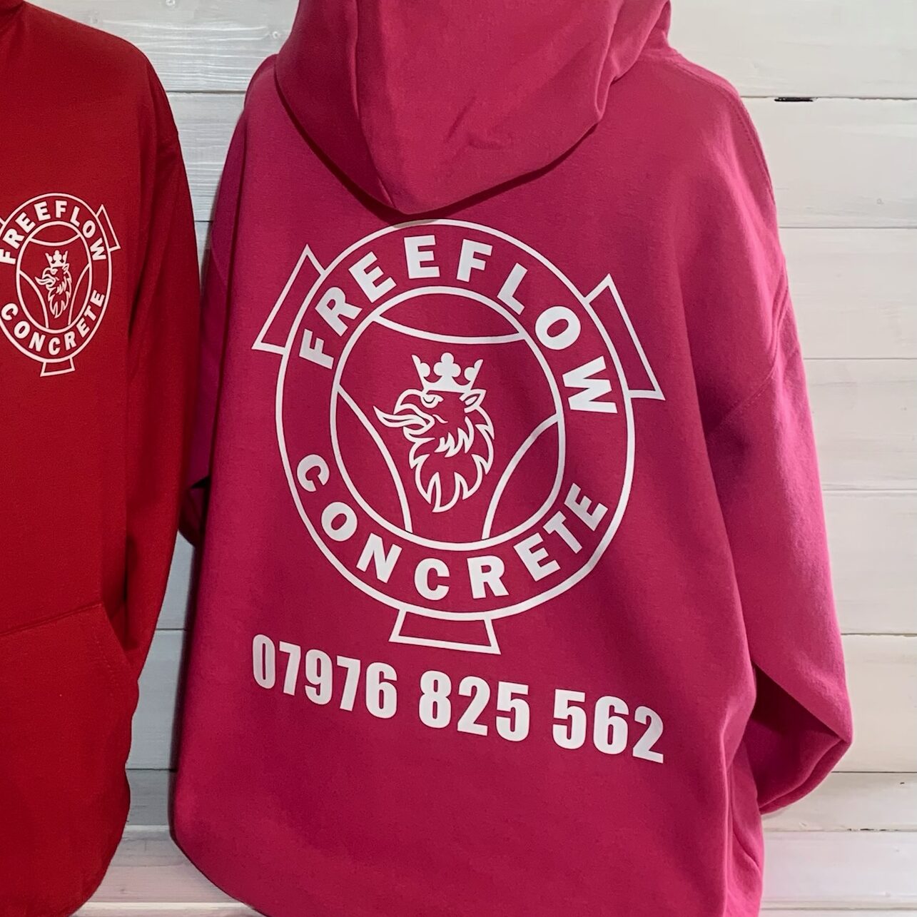 Two red hoodies with FREEFLOW CONCRETE printed on them by B-Stitch embroidery and printing in Worcestershire displayed against a white wooden background